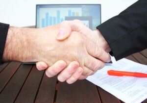 Professionals shaking hand with data and contract in the background - concept of role of data in mergers and acquisitions